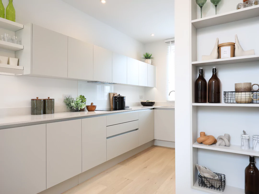 A long shot of a stylish kitchen with white work tops and ample storage.