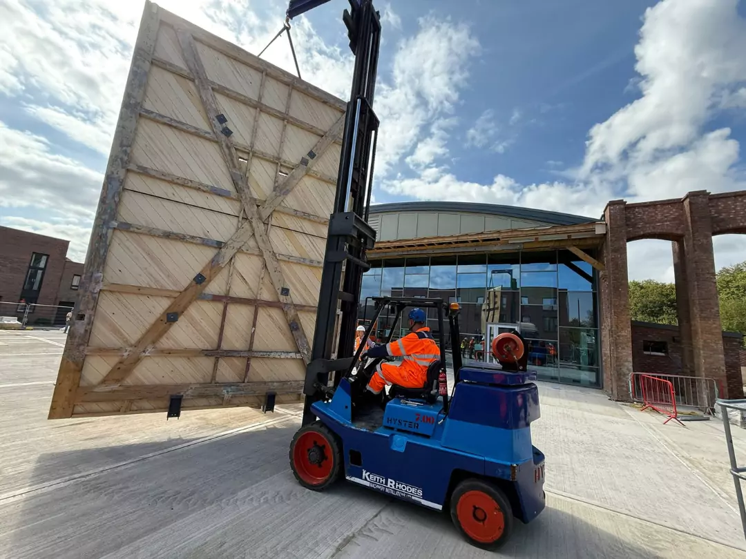 A forklift lifts a large, fully restored wooden door outside The Hangar at Brabazon, a vibrant new community hub under contruction.
