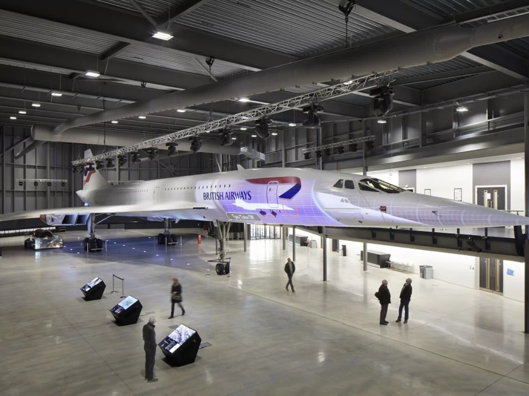 Inside Aerospace Bristol Museum, showcasing visitors walking under a sleek, white Brittish Airways plane.