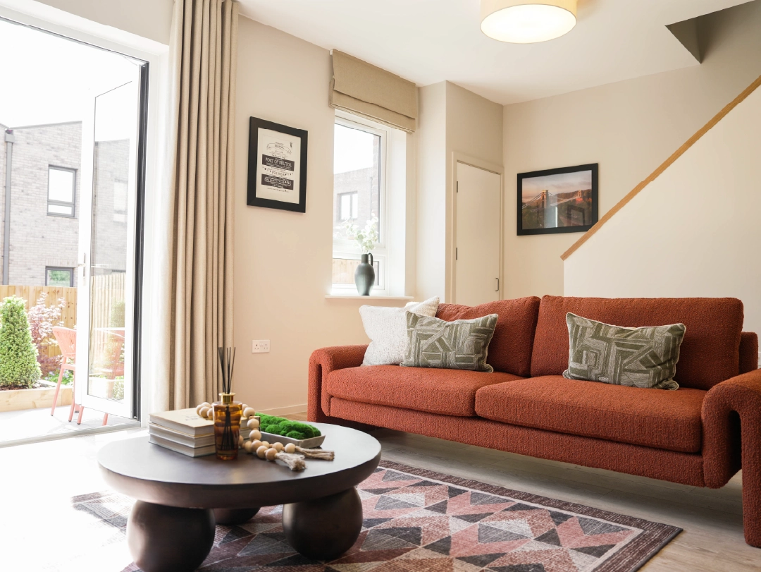 Modern living room featuring a rust-coloured sofa with patterned pillows, a round coffee table, and large windows opening to a garden.
