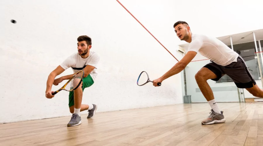 Two men playing a practise squash game on an indoor court standing in a lunge position ready to hit the squash ball.