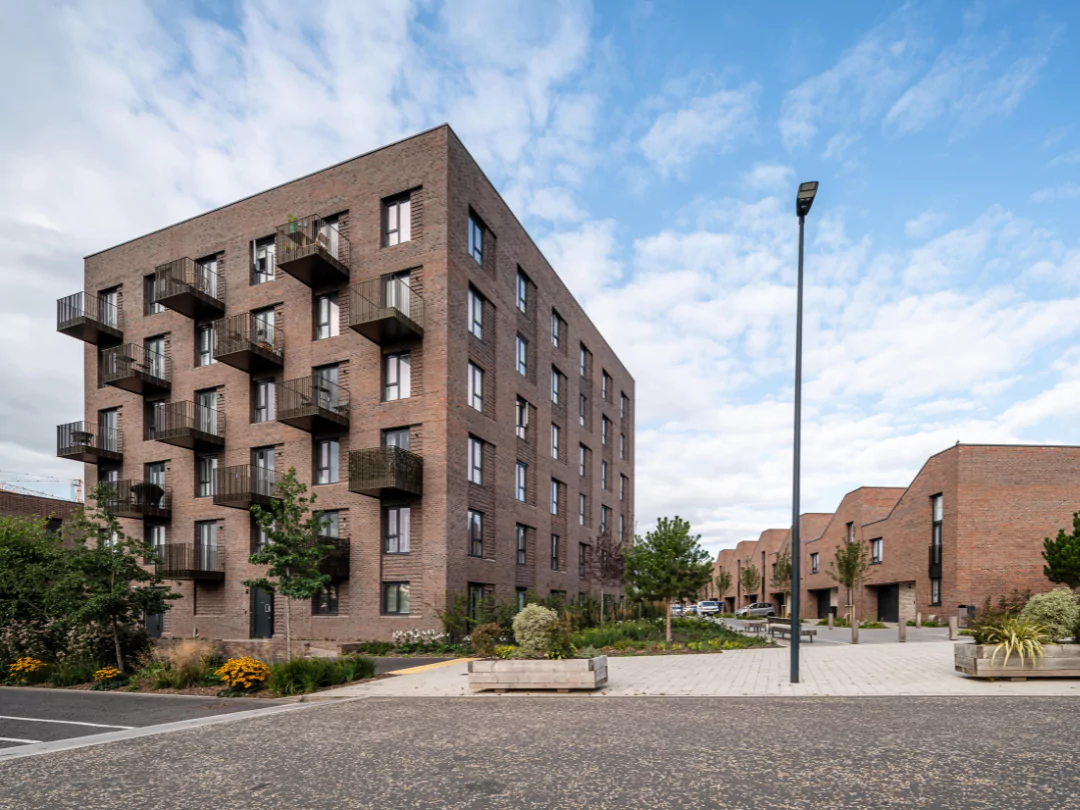 Street view of Modern apartment building at Brabazonwith large windows and balconies, surrounded by landscaped streets, trees, and a paved pedestrian walkway.