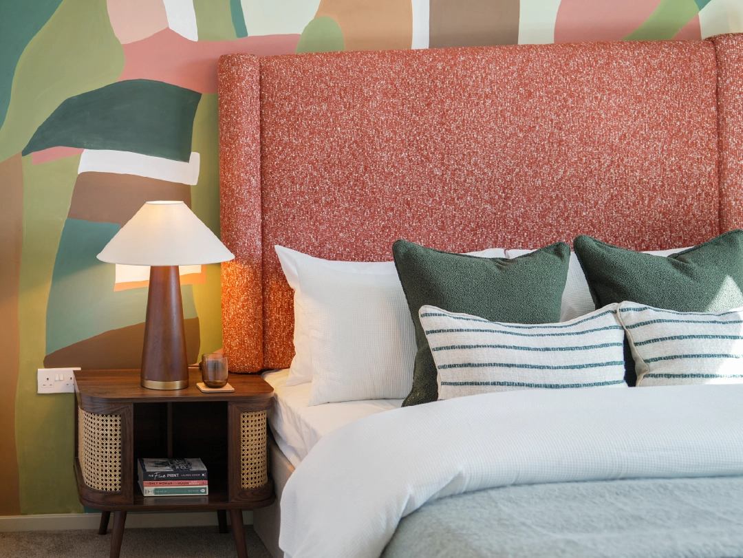 Modern primary bedroom with a textured rust-coloured headboard, green accent pillows, and a stylish bedside table with a lamp and books.