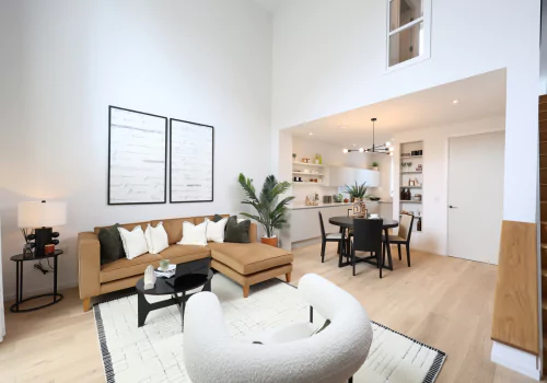 Bright and stylish living room with high ceilings, modern furniture, and a dining area leading to a built-in shelf space.