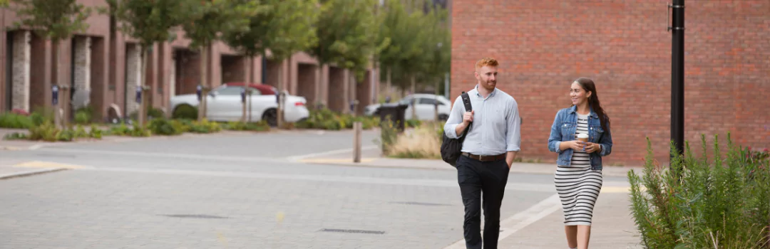 A young man and woman walk together through the streets of The Heritage District at Brabazon, showcasing intricate brickwork and wide, tree-lined streets. 