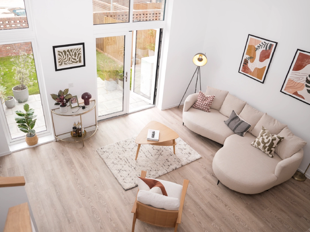 Modern living room inside The Skylark 3 bedroom home at Brabazon, with light wood floors, a beige curved sofa, and an armchair around a wooden coffee table. Large windows overlook a garden. Bright, airy ambiance.