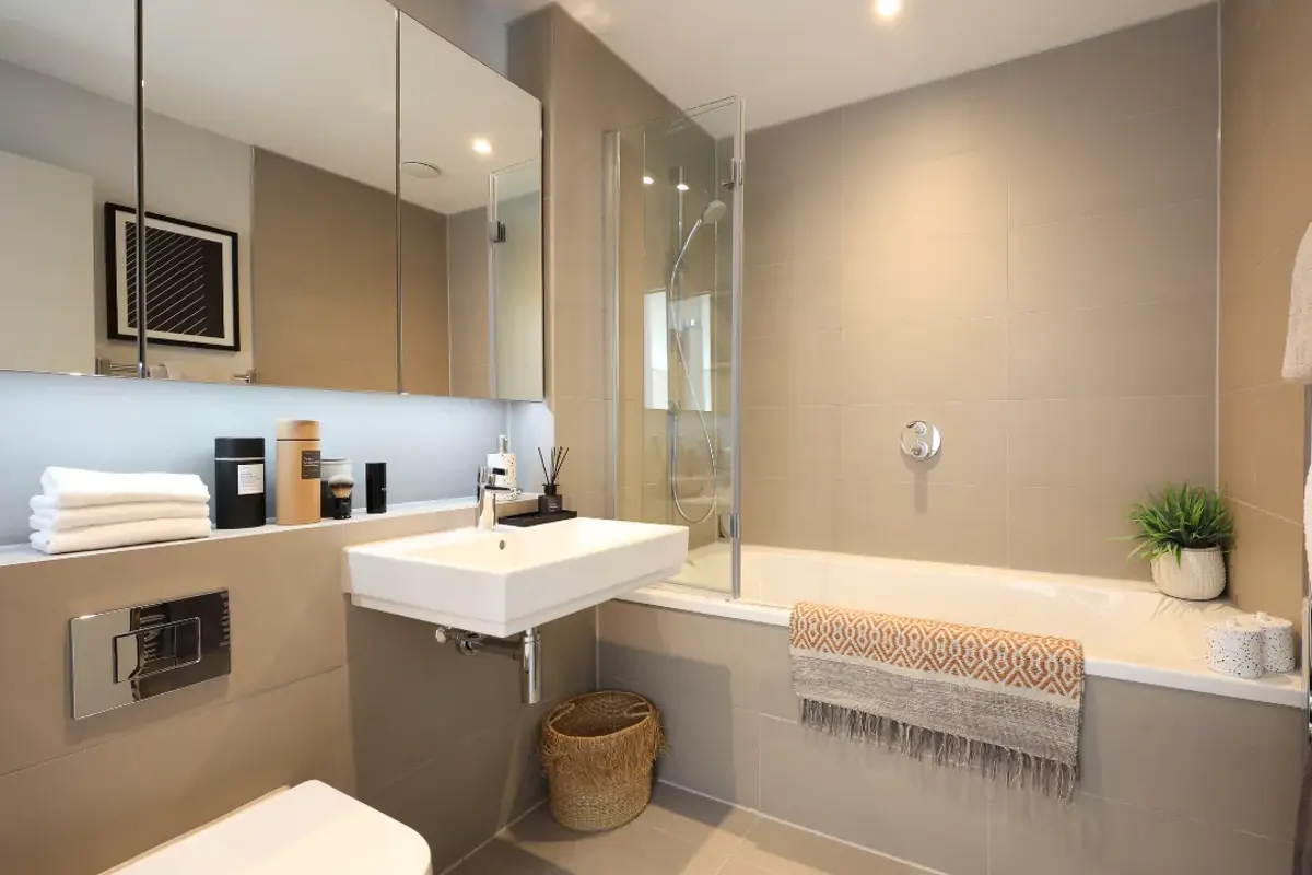 A wide angle of the family bathroom with added extras such as the large mirrored storage units and faux plants.