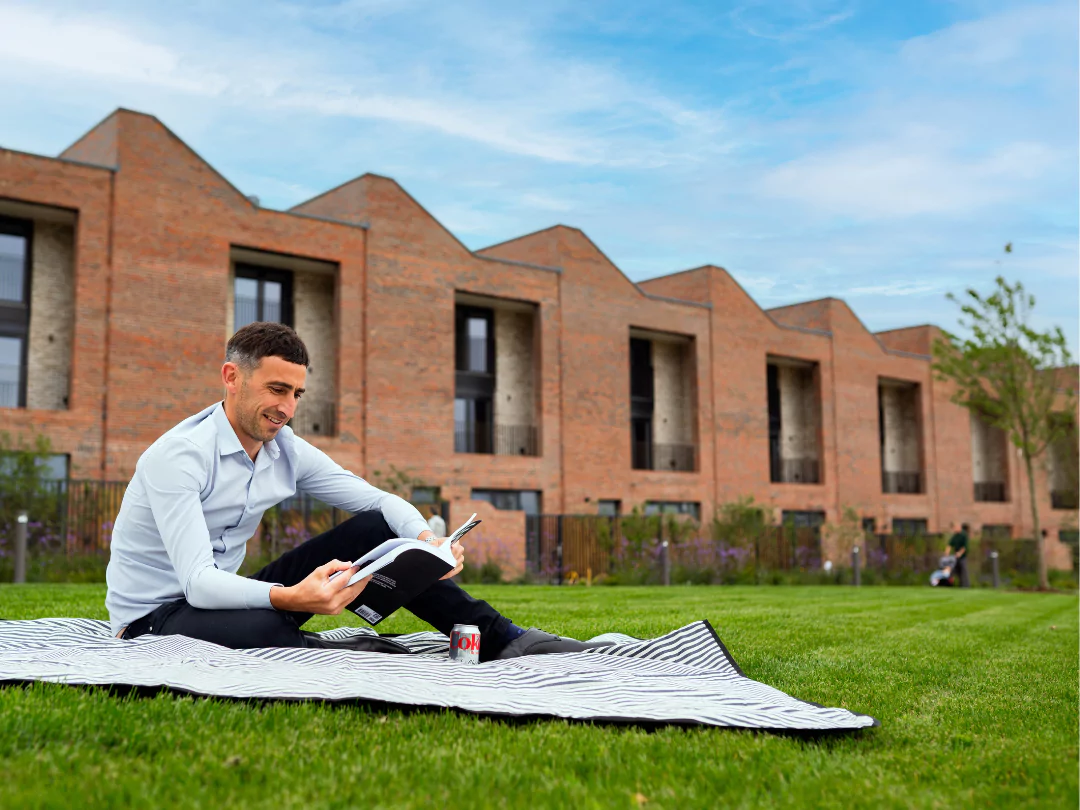 Man sitting on a picnic blanket reading a book in a green space at Brabazon Bristol