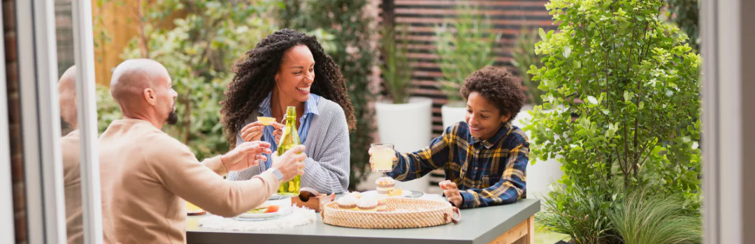 A family enjoying a meal together on a patio table in their back yard table, surrounded by greenery.