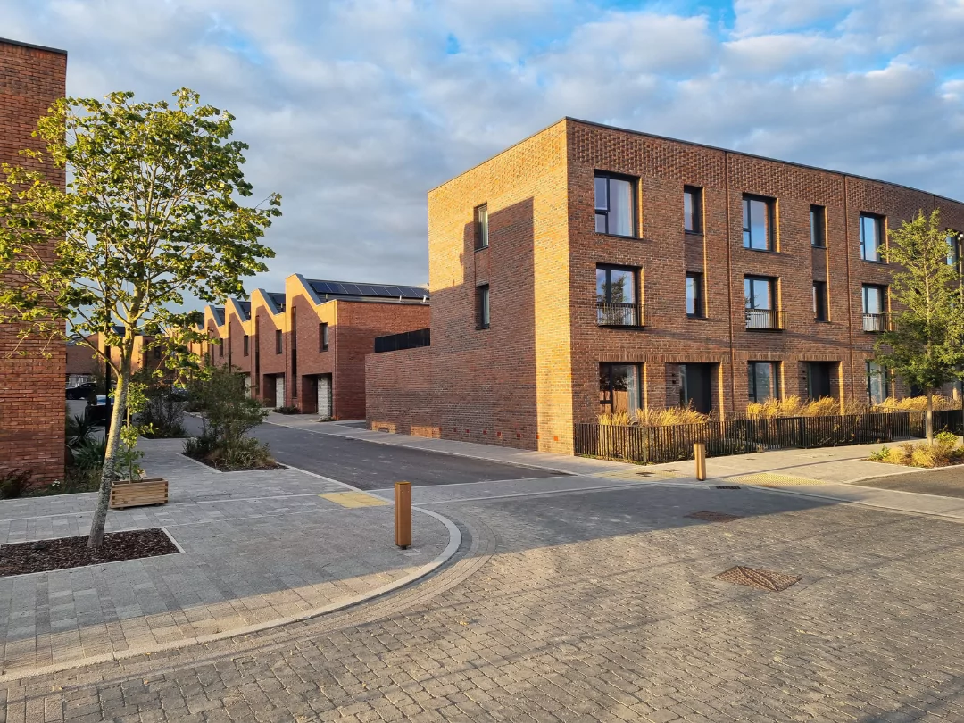 Modern residential street with contemporary brick townhouses, large windows, and landscaped surroundings, illuminated by warm sunlight in the morning. 